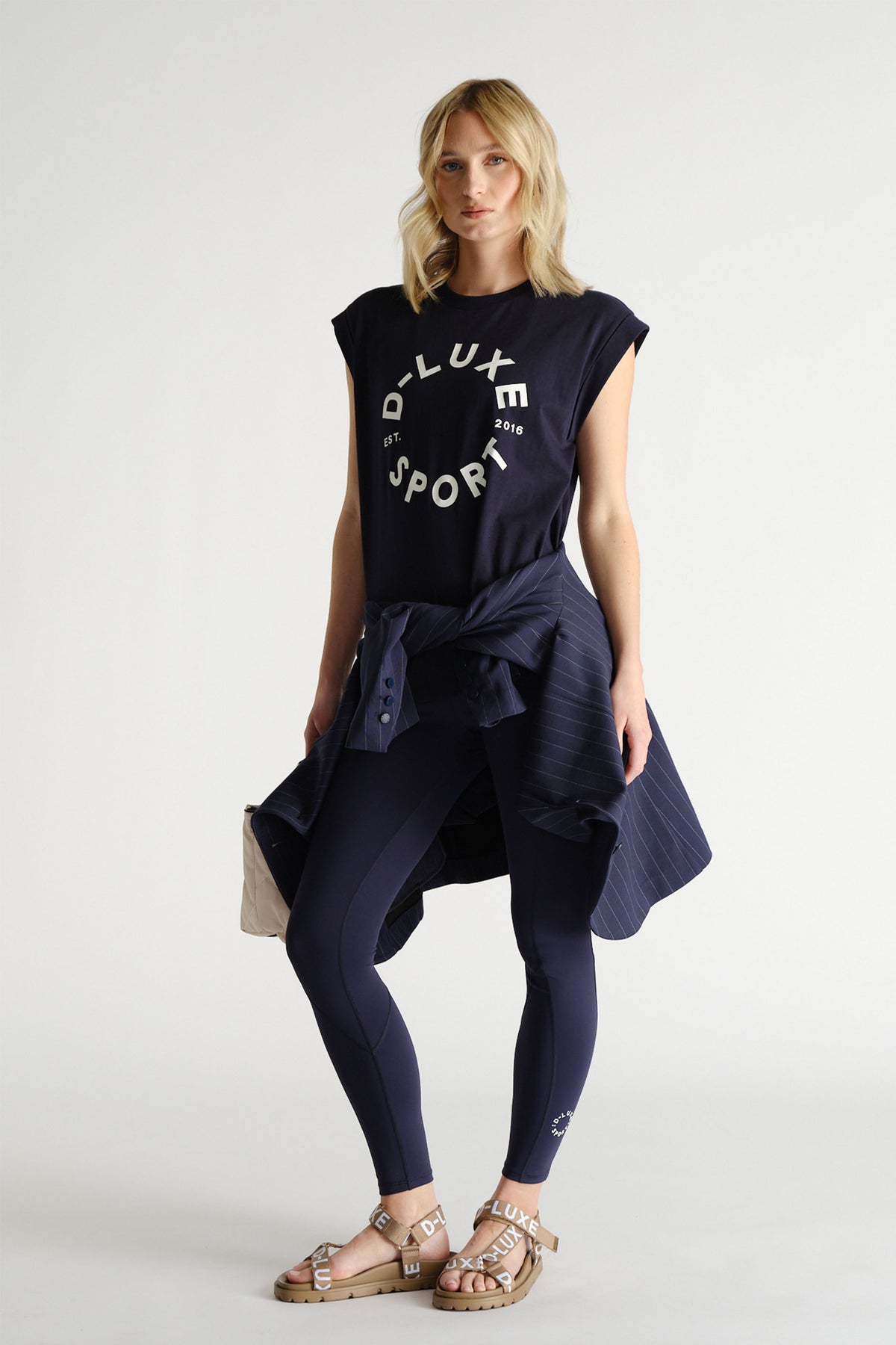 Woman styled in navy graphic tank paired with matching leggings and a pinstriped jacket tied at the waist