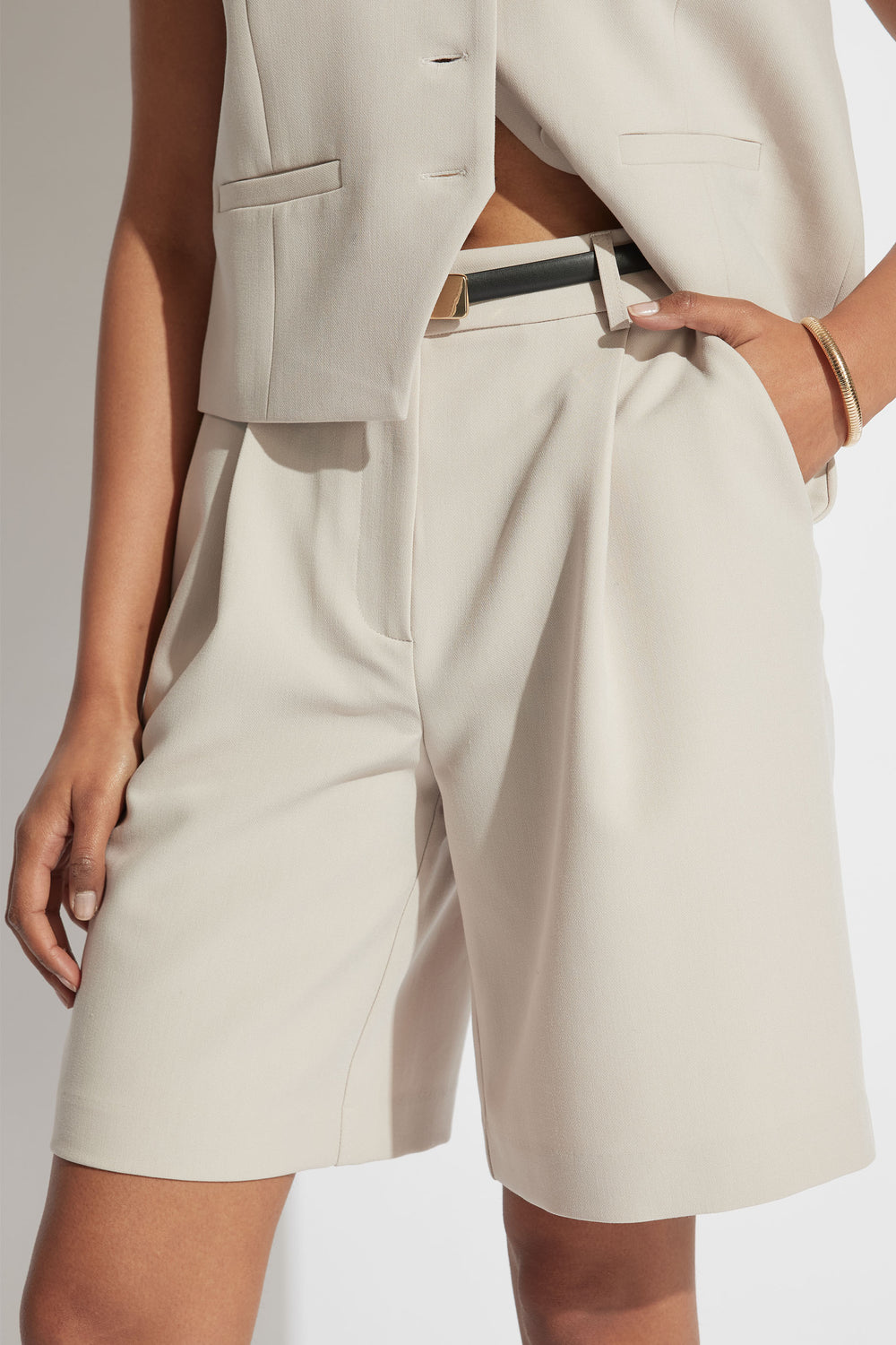 Woman wearing tailored cream longline shorts with high waist and front pleats styled with a sleeveless blazer vest