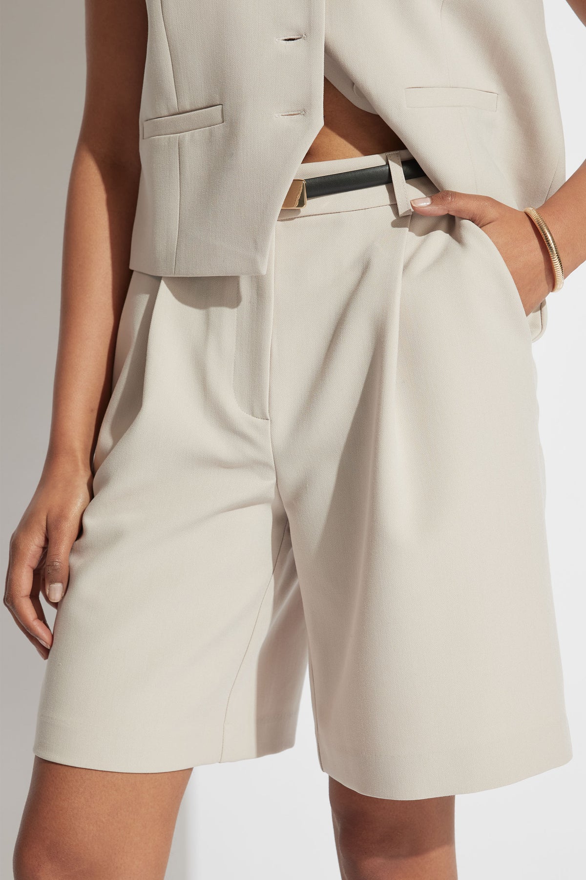 Woman wearing tailored cream longline shorts with high waist and front pleats styled with a sleeveless blazer vest