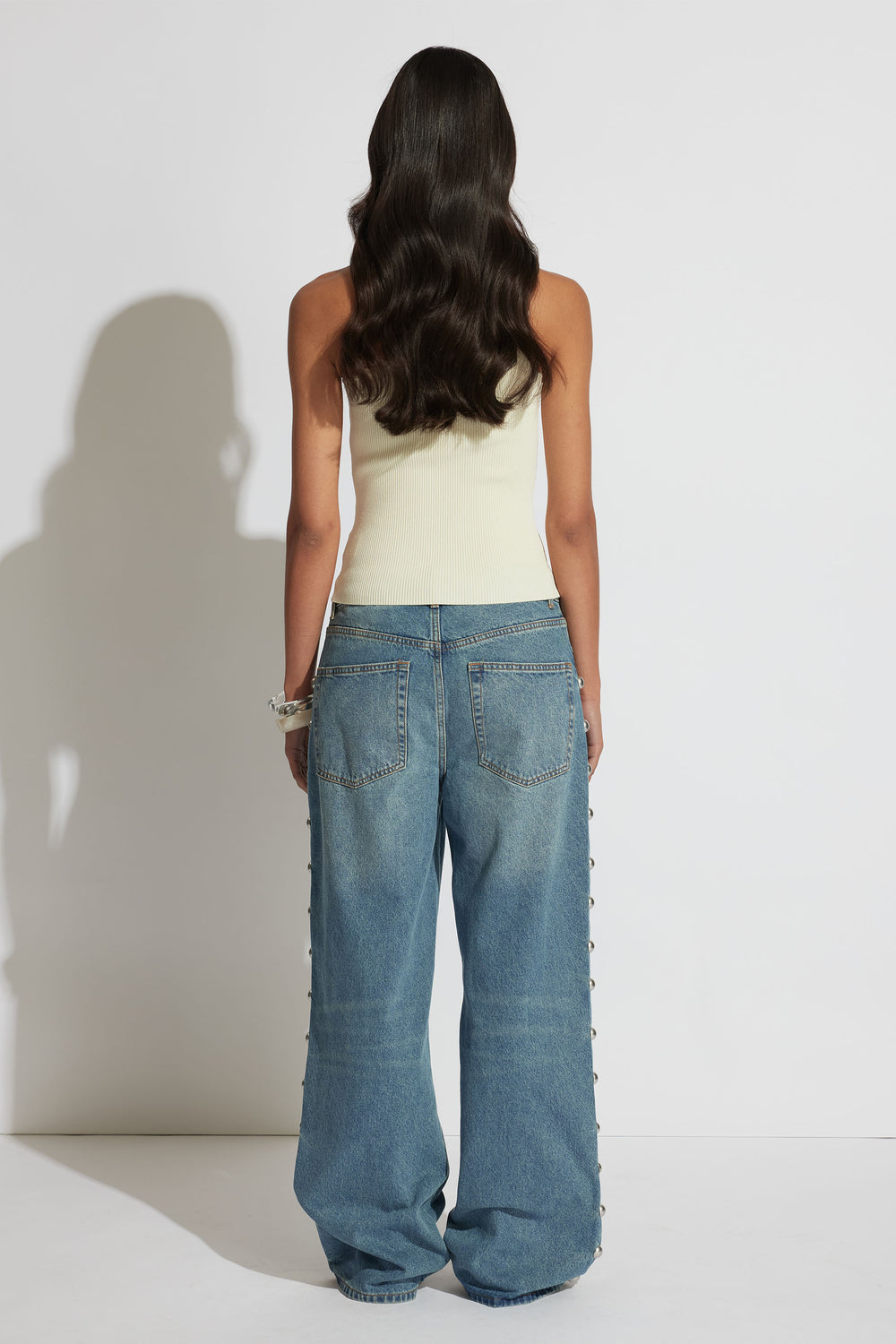 Woman wearing a cream one-shoulder tank paired with relaxed wide-leg denim jeans, shown from the back.