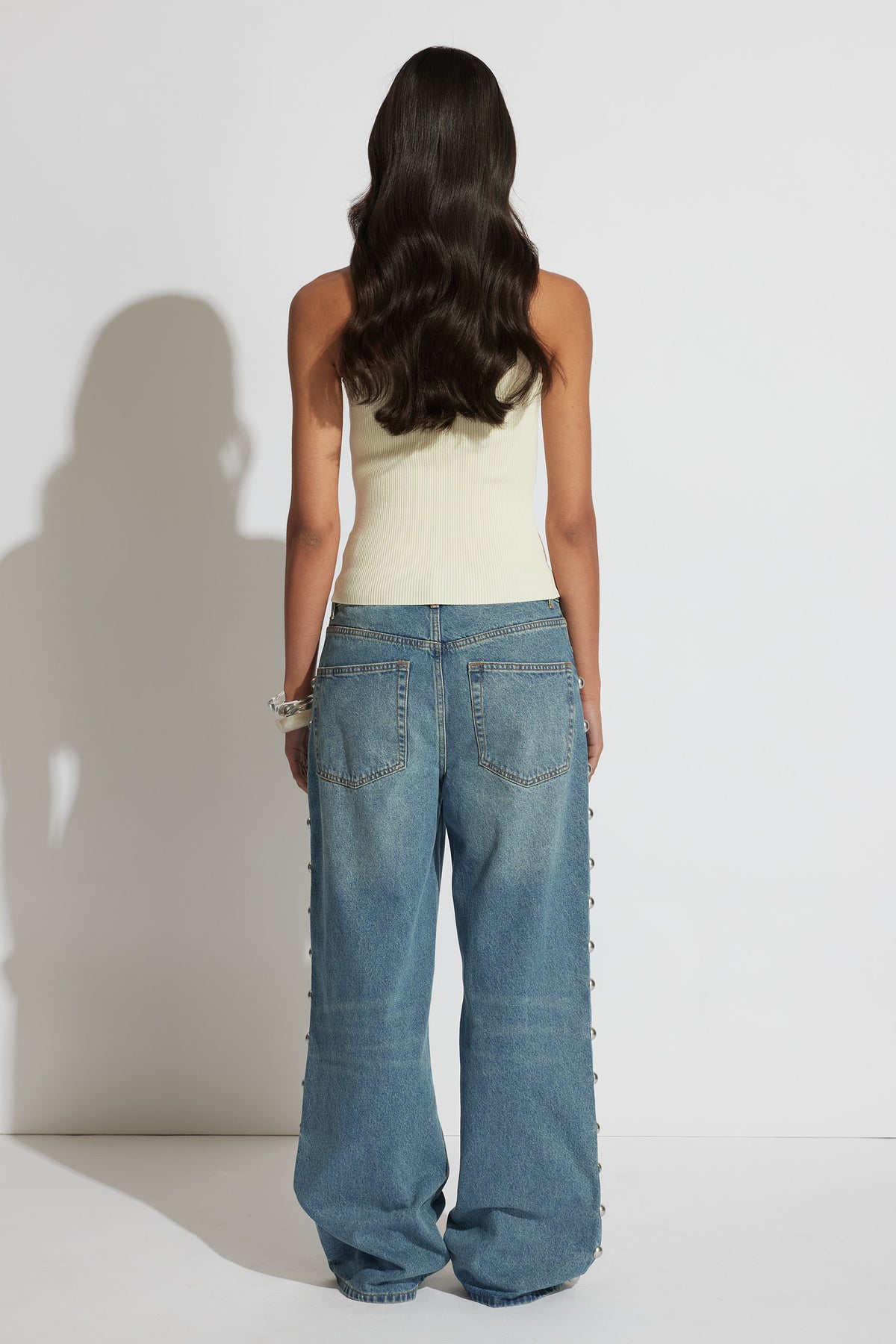 Woman wearing a cream one-shoulder tank paired with relaxed wide-leg denim jeans, shown from the back.