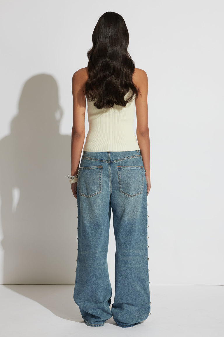 Woman wearing a cream one-shoulder tank paired with relaxed wide-leg denim jeans, shown from the back.