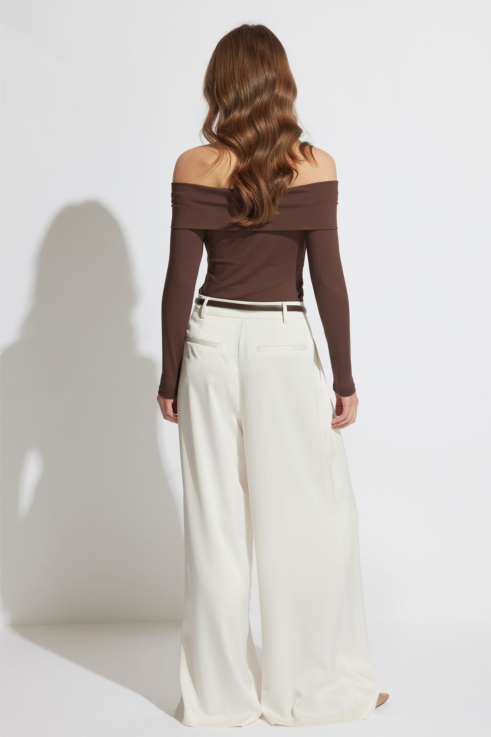 Woman with loose waves wearing an off-shoulder brown top paired with high-waisted wide-leg cream trousers