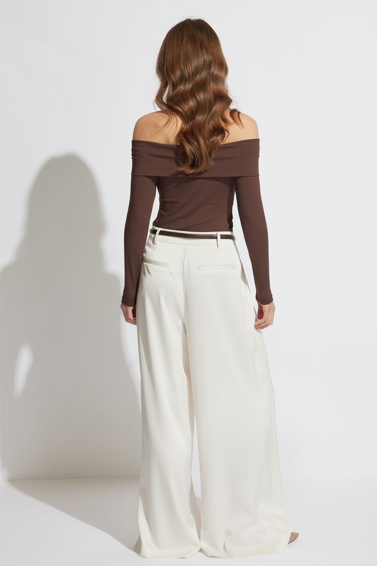 Woman with loose waves wearing an off-shoulder brown top paired with high-waisted wide-leg cream trousers