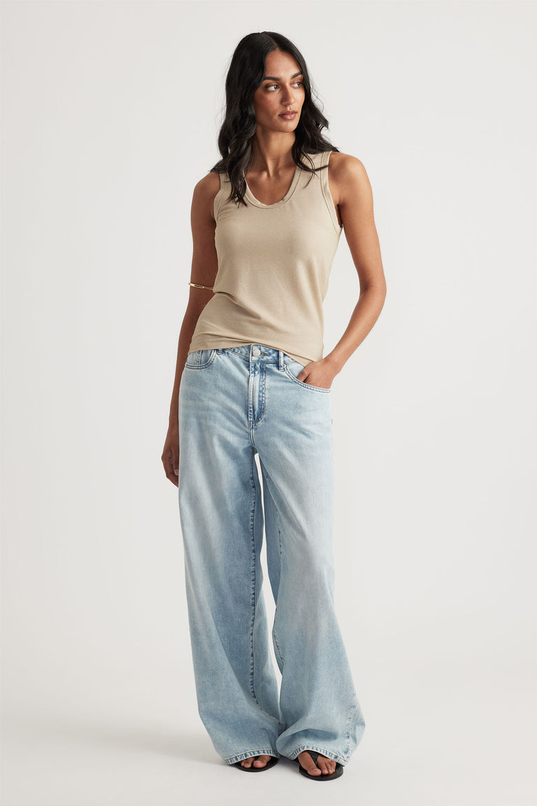 Woman wearing a neutral sleeveless tank paired with light wash wide-leg jeans and black sandals in a minimalist studio setting
