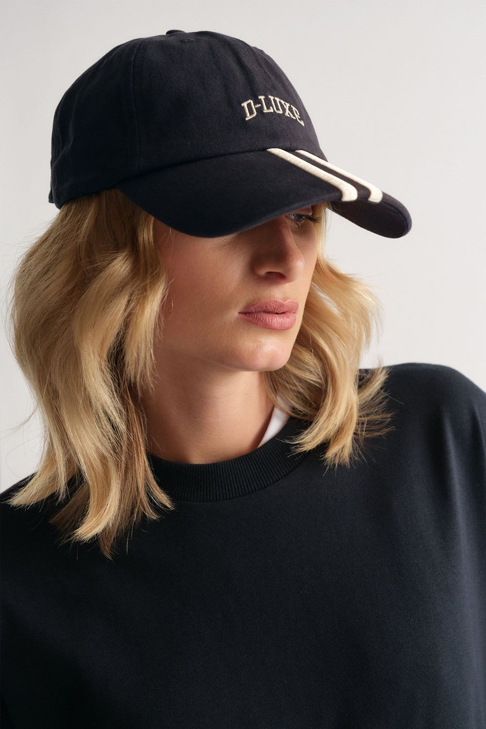 Woman wearing a navy cap with cream stripe details and D-Luxe embroidery, paired with a black crew neck top