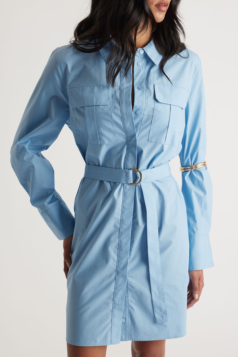 Woman wearing a belted light blue shirt dress with chest pockets and long sleeves in a relaxed fit style