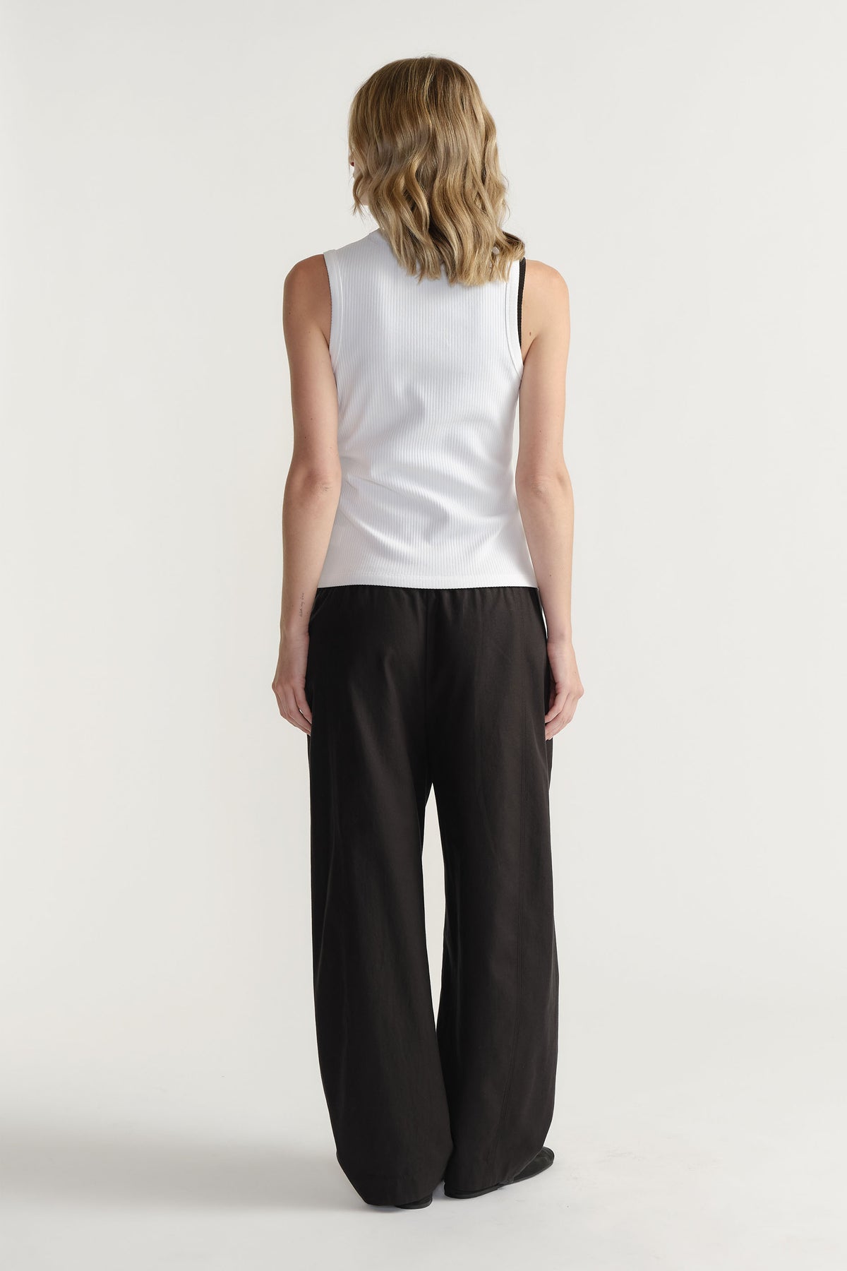 Woman wearing a white ribbed scoop tank paired with loose black wide-leg pants for a relaxed everyday look