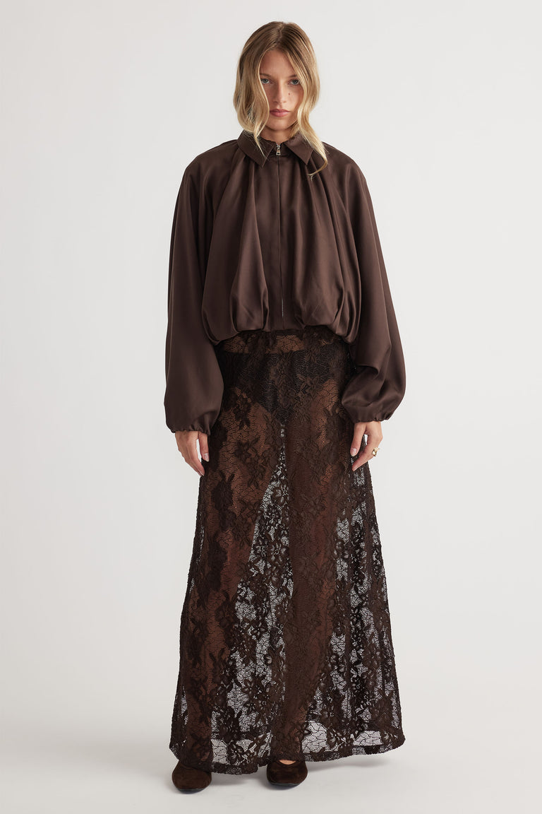 Woman wearing a flowing dark brown lace maxi skirt paired with a loose, balloon-sleeve jacket for effortless style.