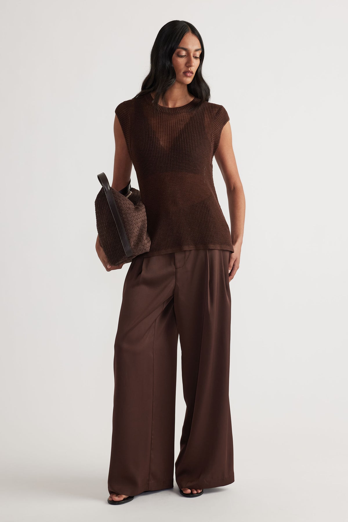 Woman wearing a sleeveless brown knit tank with wide-leg chocolate brown trousers and carrying a textured tote bag