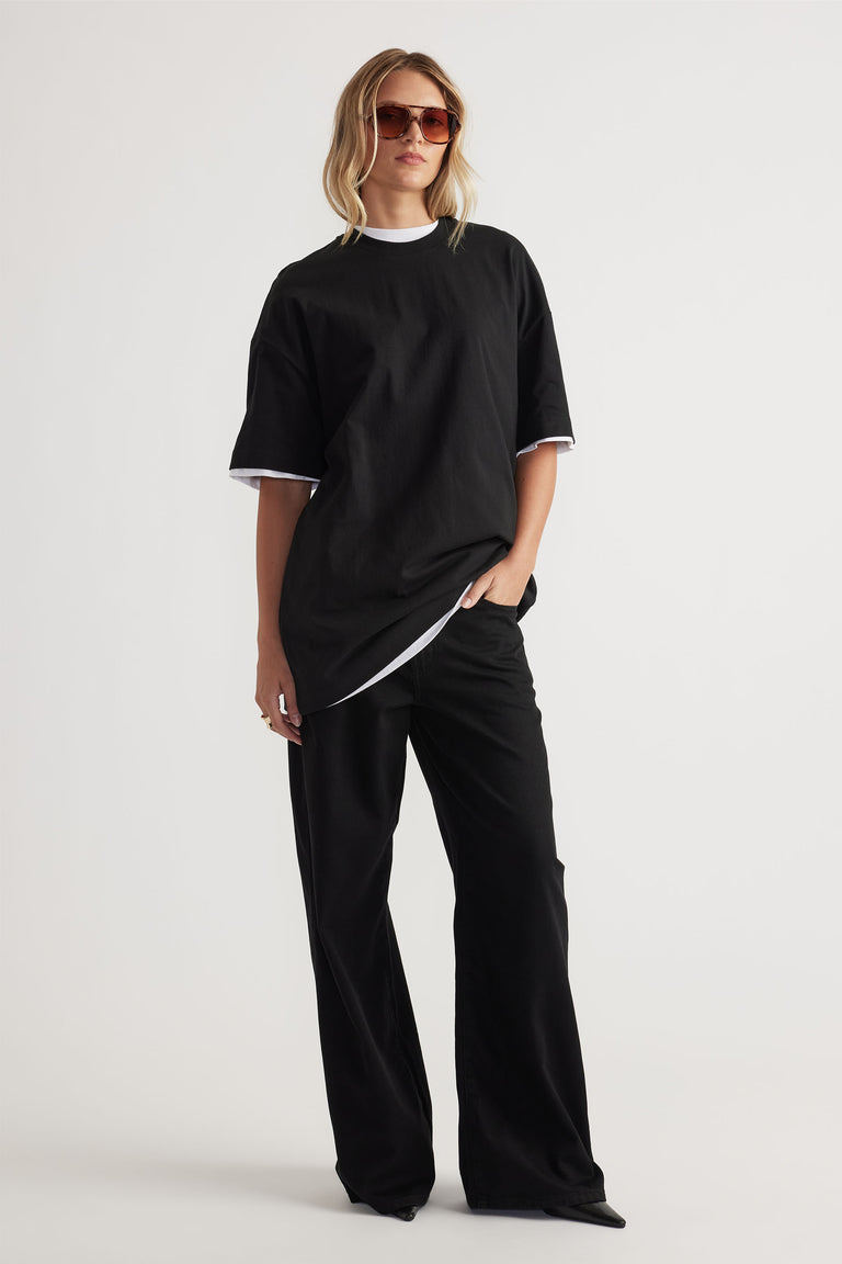 Front view of model wearing black Kayla Longline Tee layered over white top with wide-leg black pants by Decjuba Australian brand