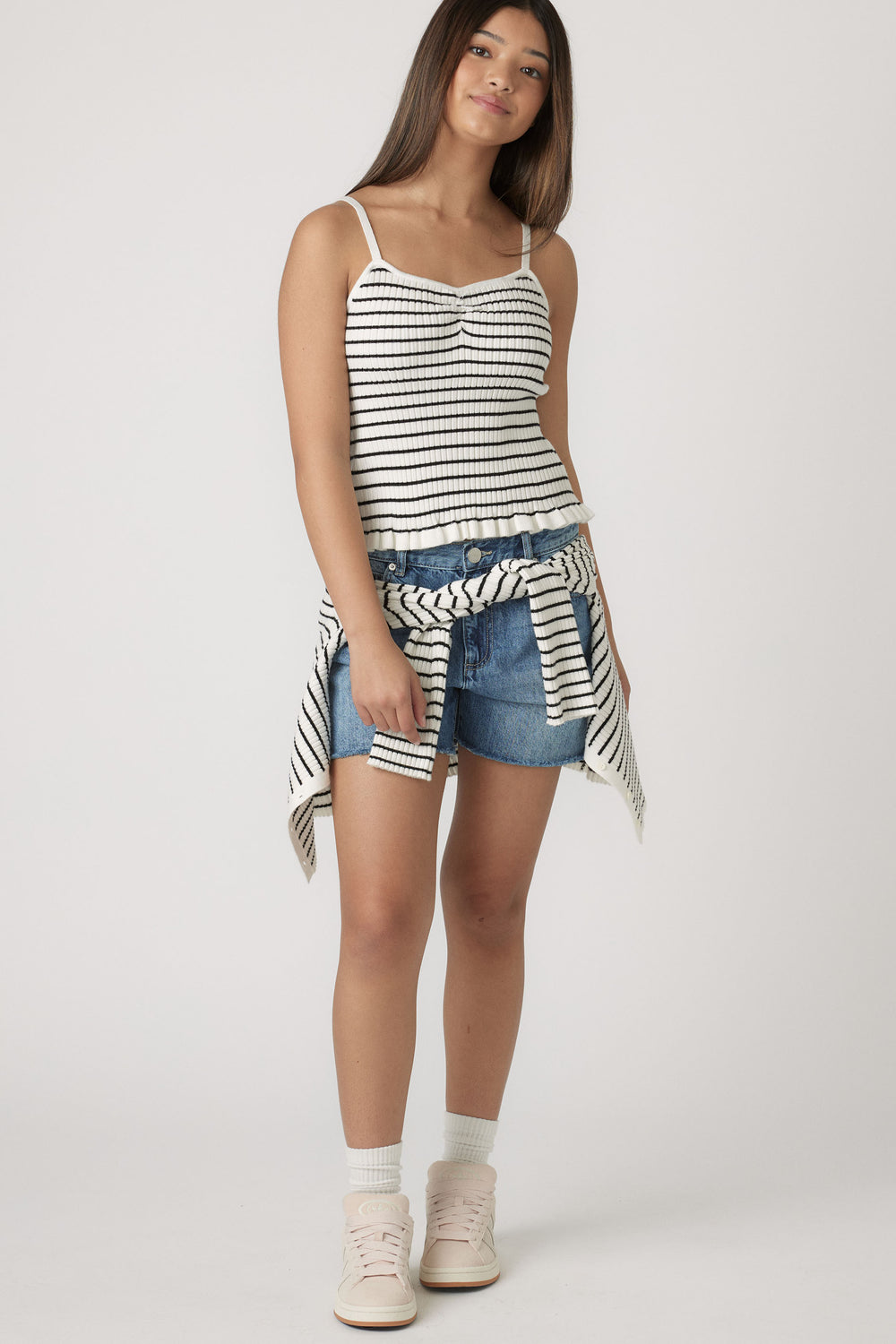 Girl wearing a striped frill tank top with denim shorts and a matching striped sweater tied around the waist