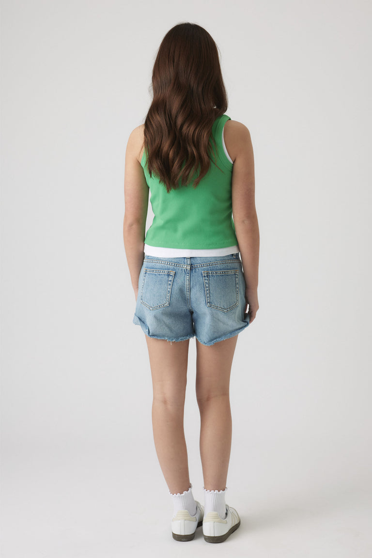 Girl wearing a green tank layered over a white tee paired with light blue denim shorts and white sneakers.