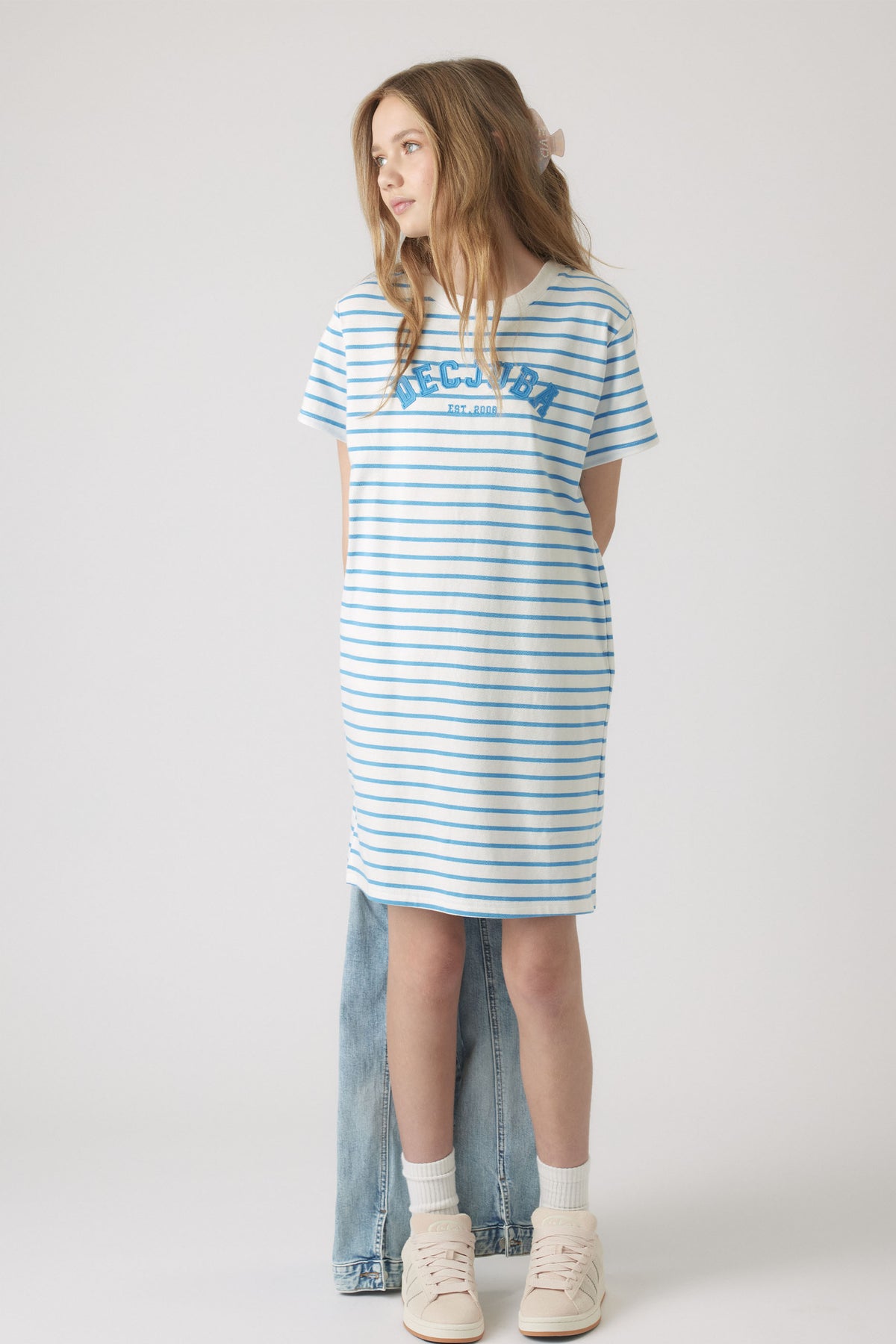 Girl wearing a relaxed striped rugby tee dress in soft blue and white, styled with light sneakers and white socks.