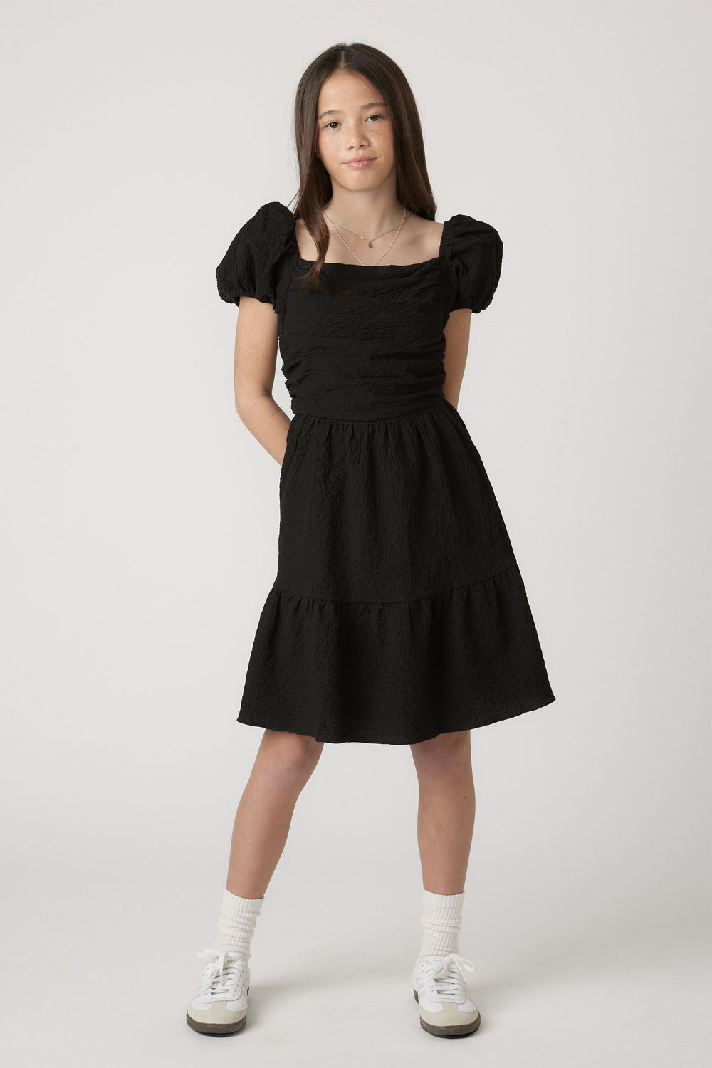 Girl wearing Girls Evie Textured Mini Dress in black with puff sleeves, styled casually by Decjuba Australian fashion brand