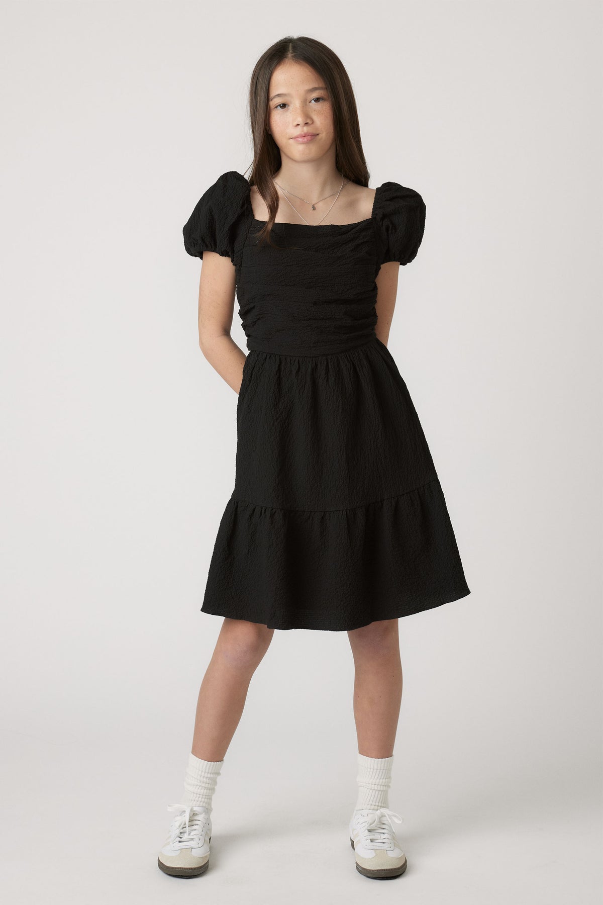 Girl wearing Girls Evie Textured Mini Dress in black with puff sleeves, styled casually by Decjuba Australian fashion brand