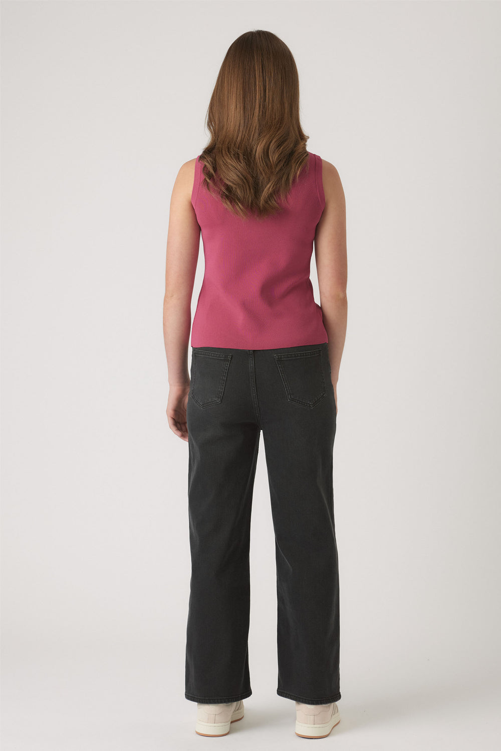 Girl shown from behind wearing a berry knit vest paired with relaxed black denim jeans and white sneakers against a neutral backdrop