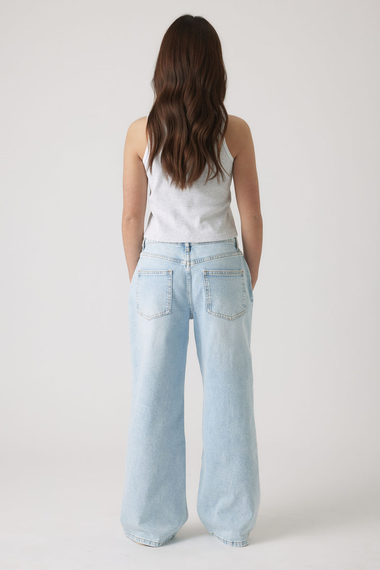 Girl wearing a light grey tank top paired with faded wide-leg light blue denim jeans, seen from the back.