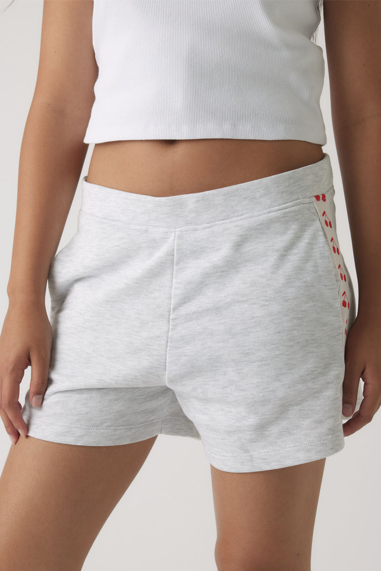 Girl wearing light grey sweat shorts with a relaxed fit and subtle red cherry print detail on the side panel