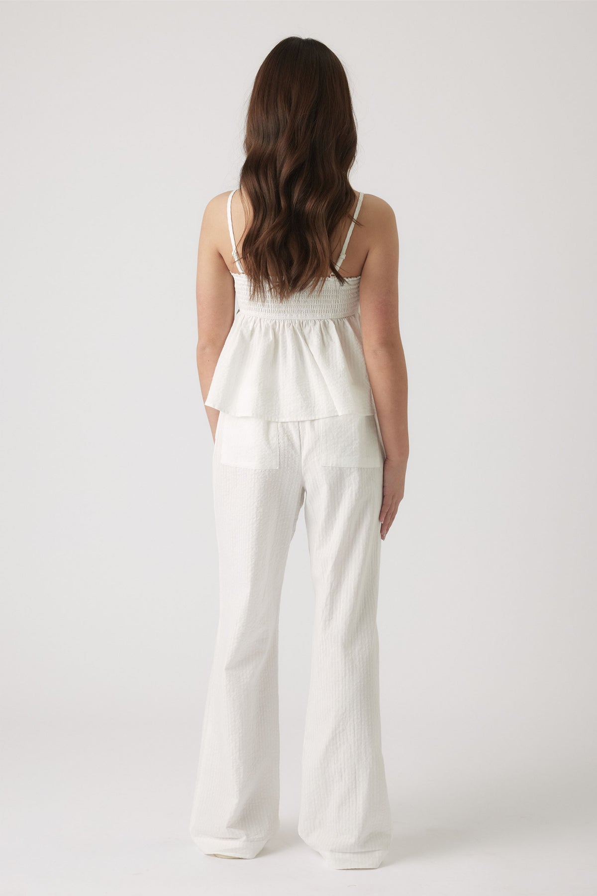 Girl wearing white textured wide-leg pants paired with a sleeveless top featuring thin straps and a gathered waist.