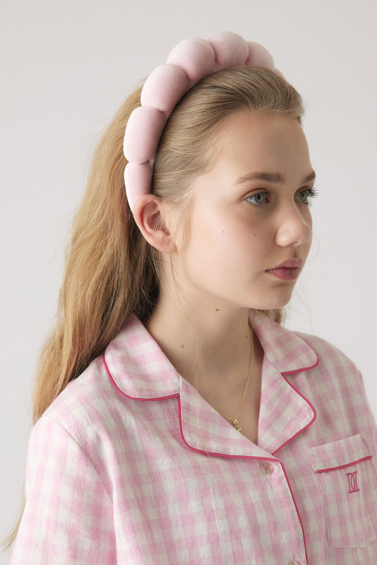 Young girl wearing a plush pink padded headband paired with a soft pink gingham pajama top with contrast piping.