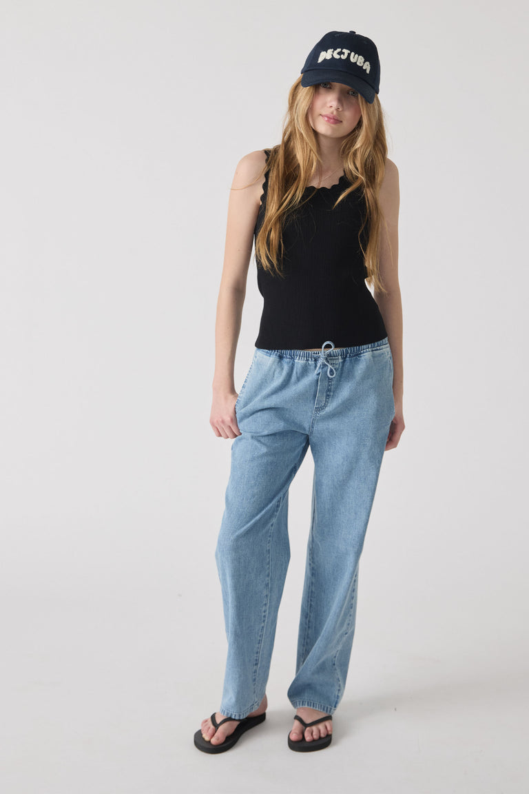 Girl wearing a casual black tank top with scalloped edges, light blue relaxed denim jeans, and a navy cap.