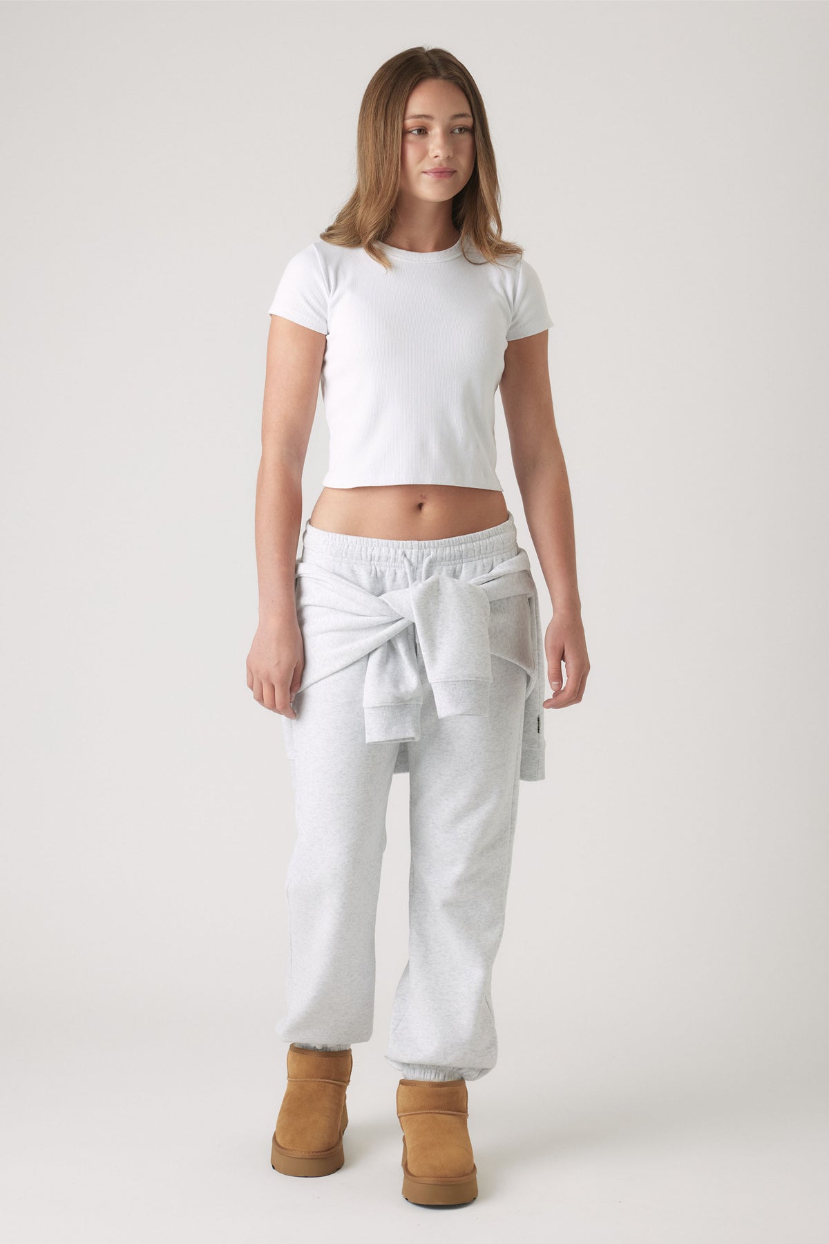 Girl wearing light grey elastic cuff track pants with a casual sweatshirt tied around the waist and tan boots