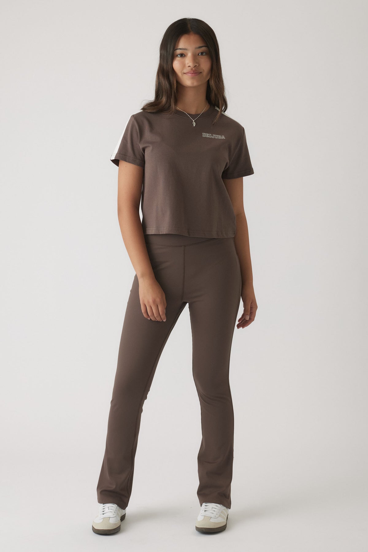 Young woman wearing mocha-colored fitted yoga pants with a matching cropped t-shirt and white sneakers
