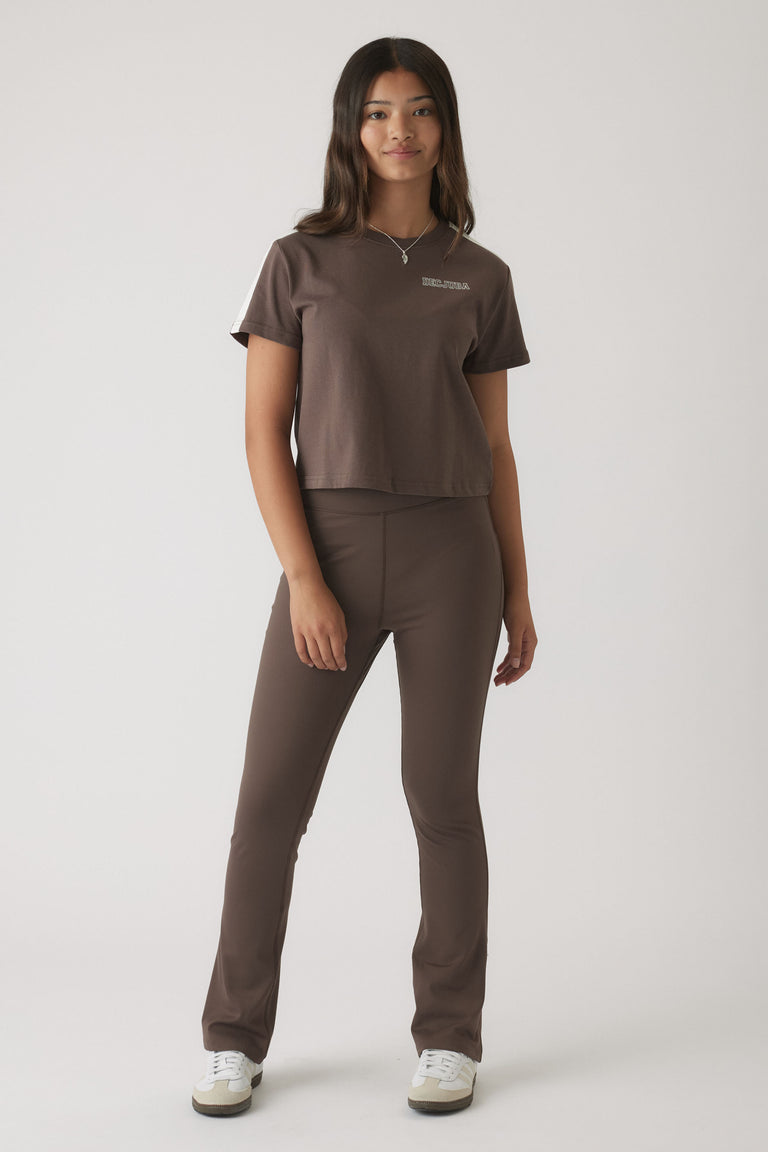 Young woman wearing mocha-colored fitted yoga pants with a matching cropped t-shirt and white sneakers