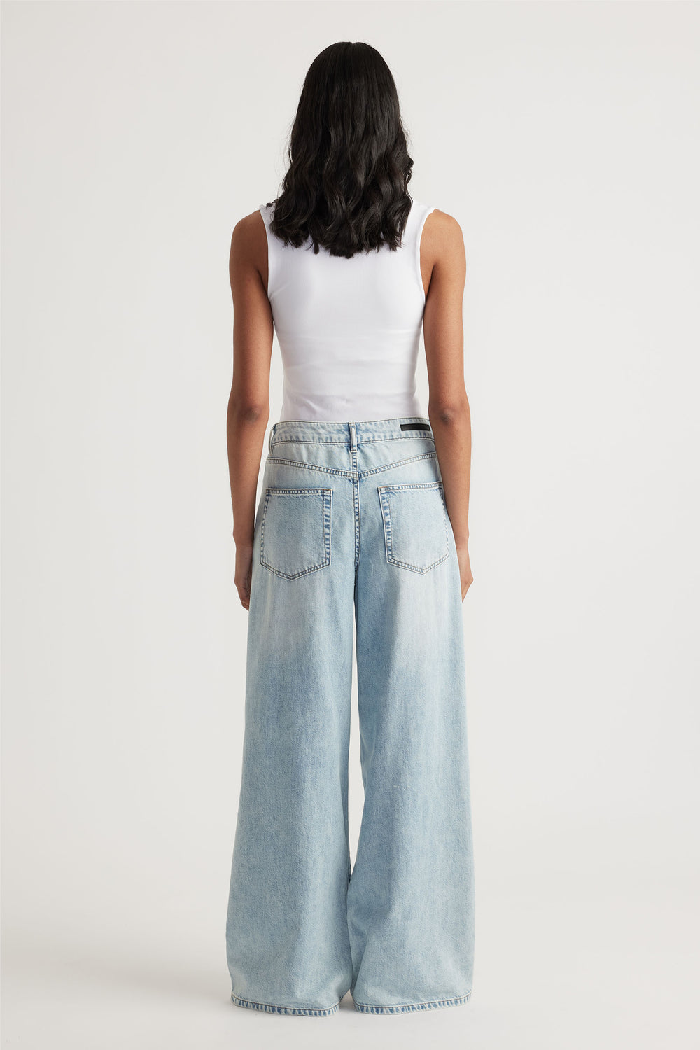 Woman wearing a white seamless scoop tank paired with light wash wide-leg denim jeans for a laid-back casual look.