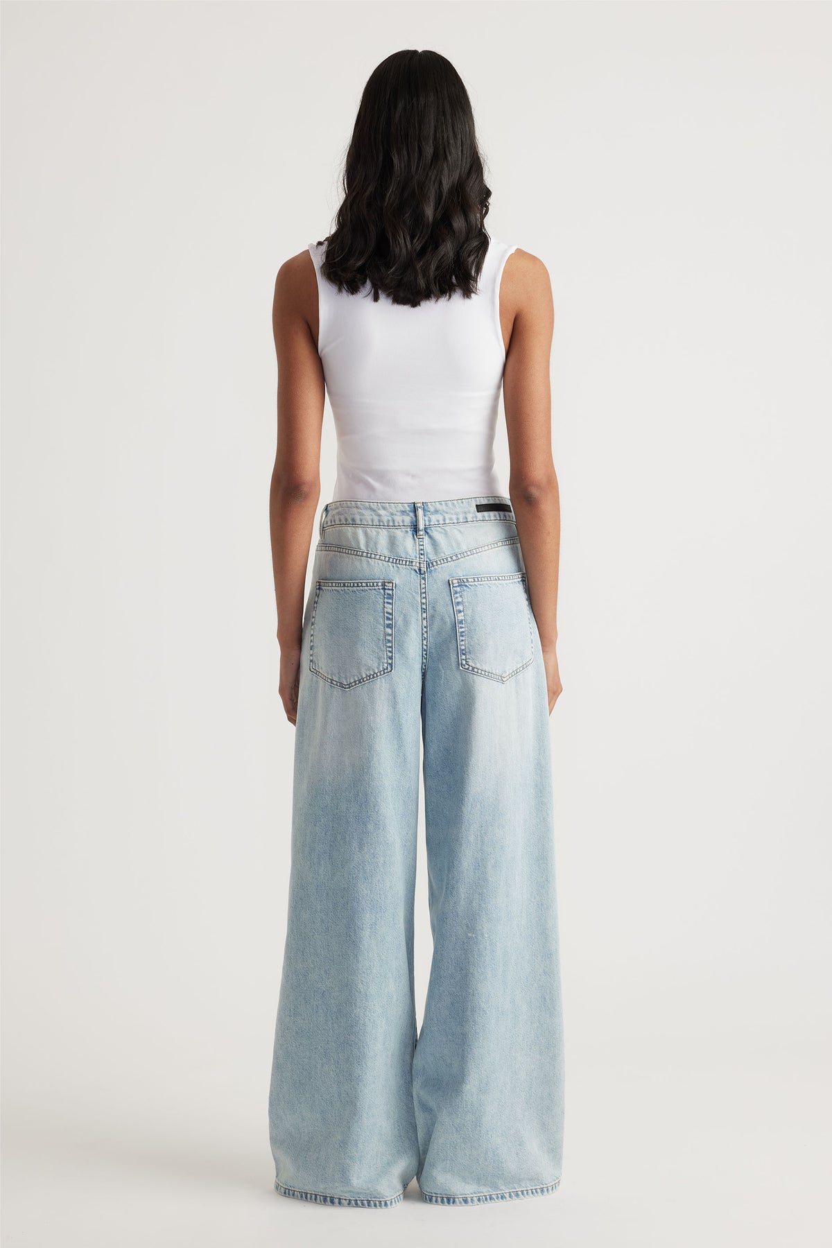 Woman wearing a white seamless scoop tank paired with light wash wide-leg denim jeans for a laid-back casual look.