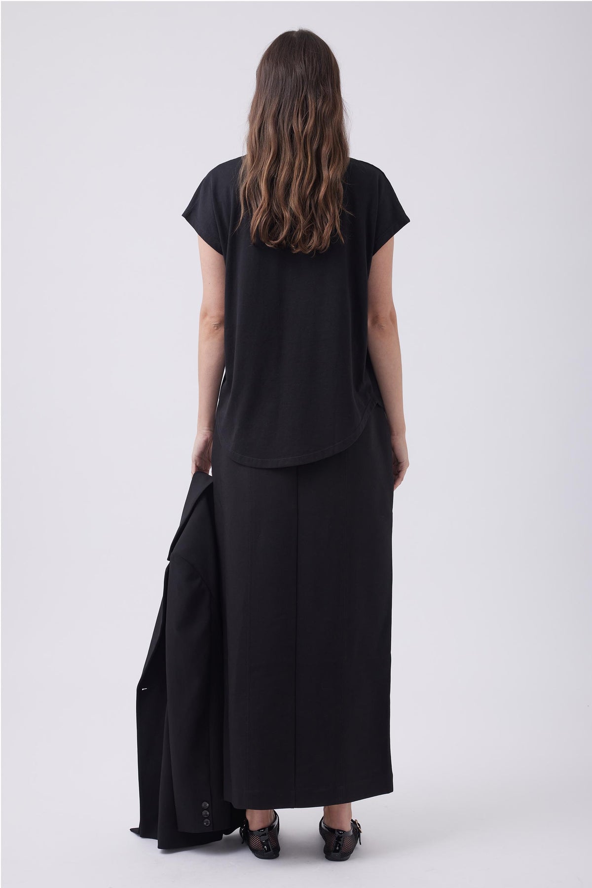 Woman wearing a relaxed black V-neck tee paired with a long black skirt, holding a matching black blazer.