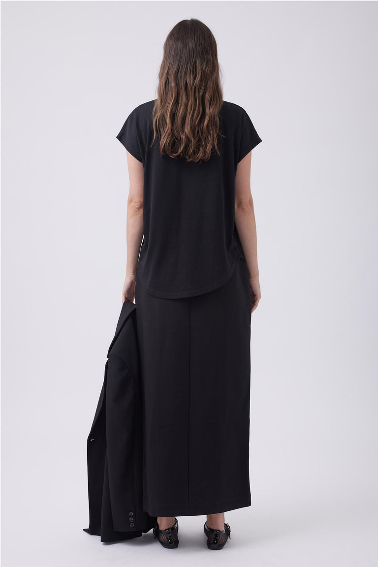 Woman wearing a relaxed black V-neck tee paired with a long black skirt, holding a matching black blazer.