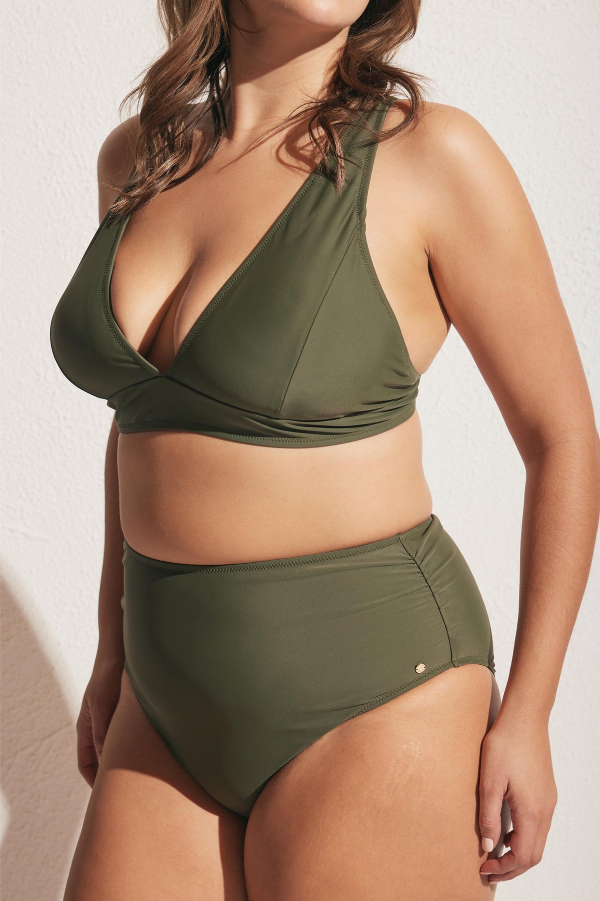 Woman wearing forest green matte triangle bikini top and high-waisted bottoms, standing against textured wall