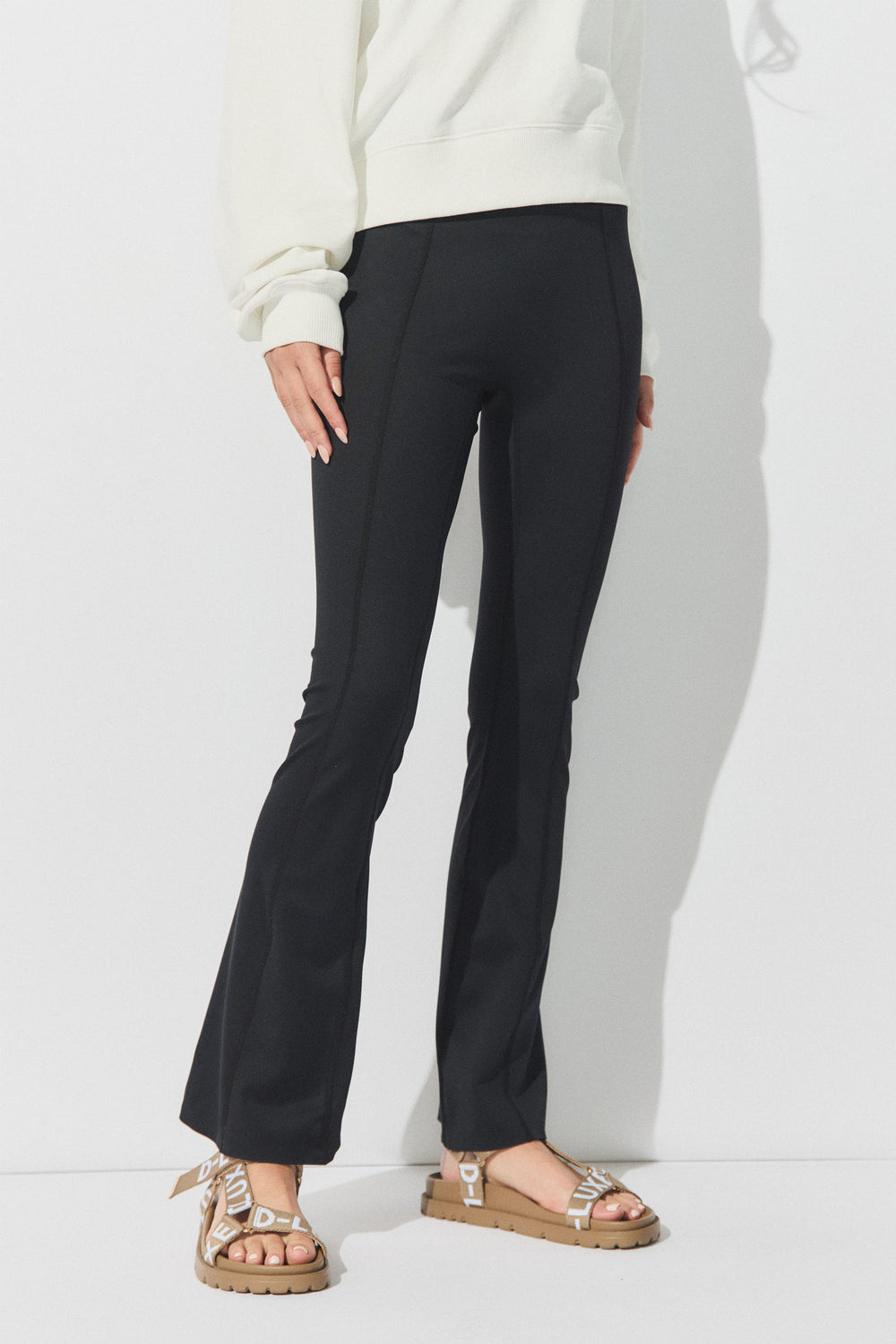 Person wearing black flare yoga leggings paired with a relaxed cream sweatshirt and beige sandals with ribbon straps