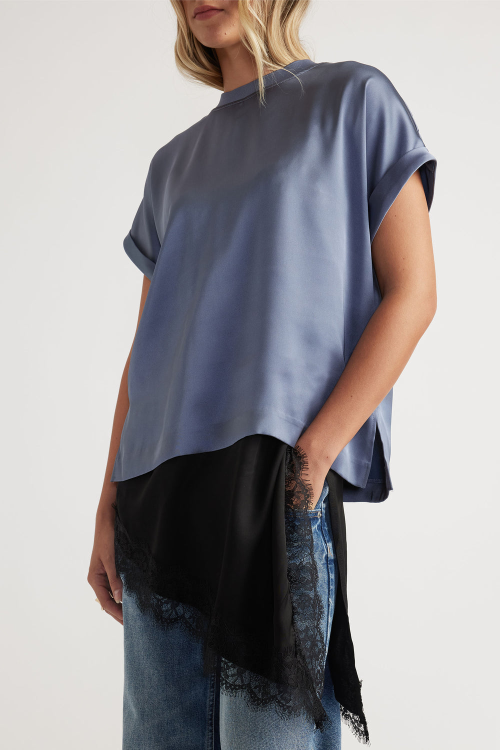 Woman wearing a loose steel blue satin tee with rolled sleeves, layered over a black lace-trimmed slip and light denim jeans.