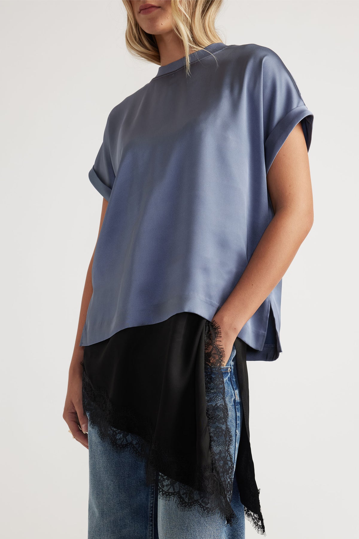 Woman wearing a loose steel blue satin tee with rolled sleeves, layered over a black lace-trimmed slip and light denim jeans.