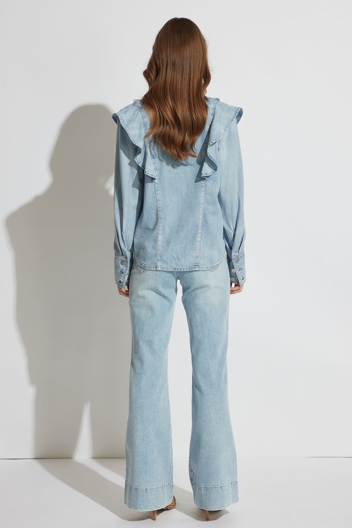 Back view of Cecilia Ruffle Denim Blouse showing ruffle detail and buttoned cuffs in gallery position 3 portrait orientation.