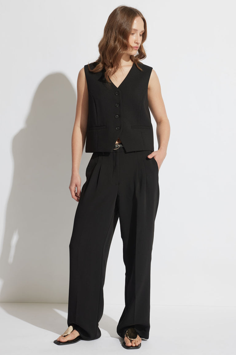 Woman wearing a black tailored vest with a V-neck and button front paired with wide-leg black trousers and sandals