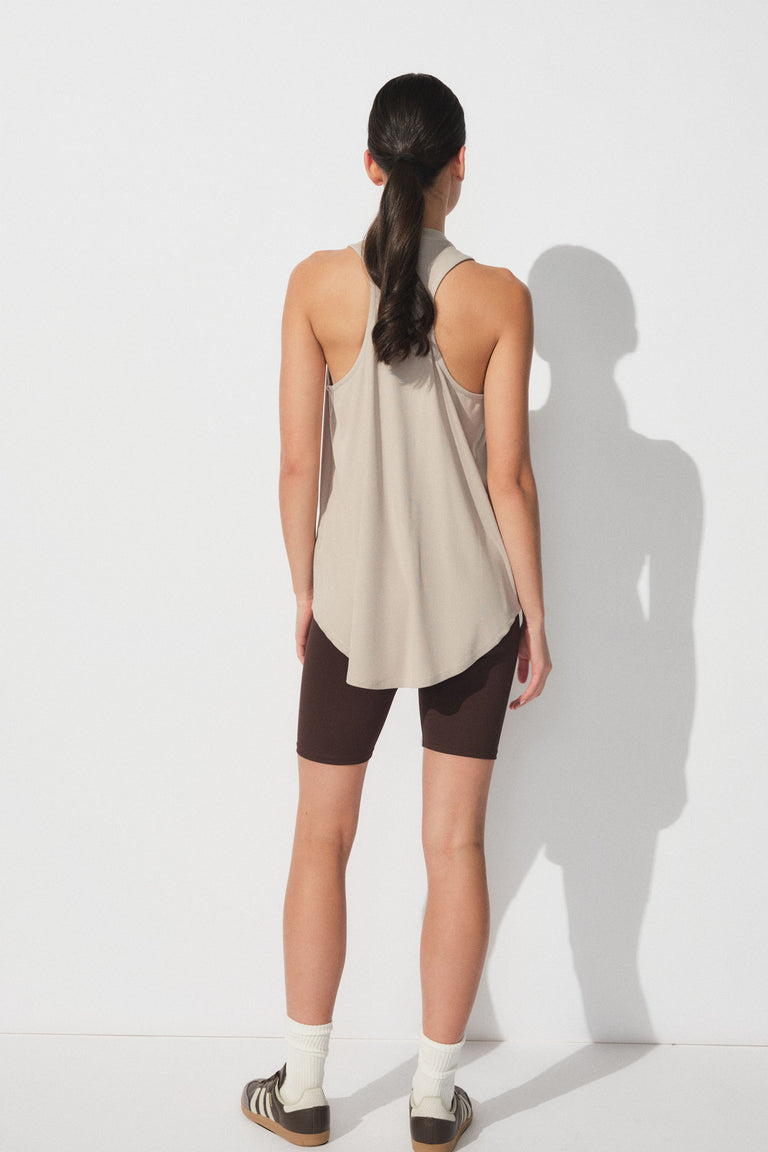 Back view of woman wearing a beige racerback bamboo tank paired with dark brown bike shorts and sneakers
