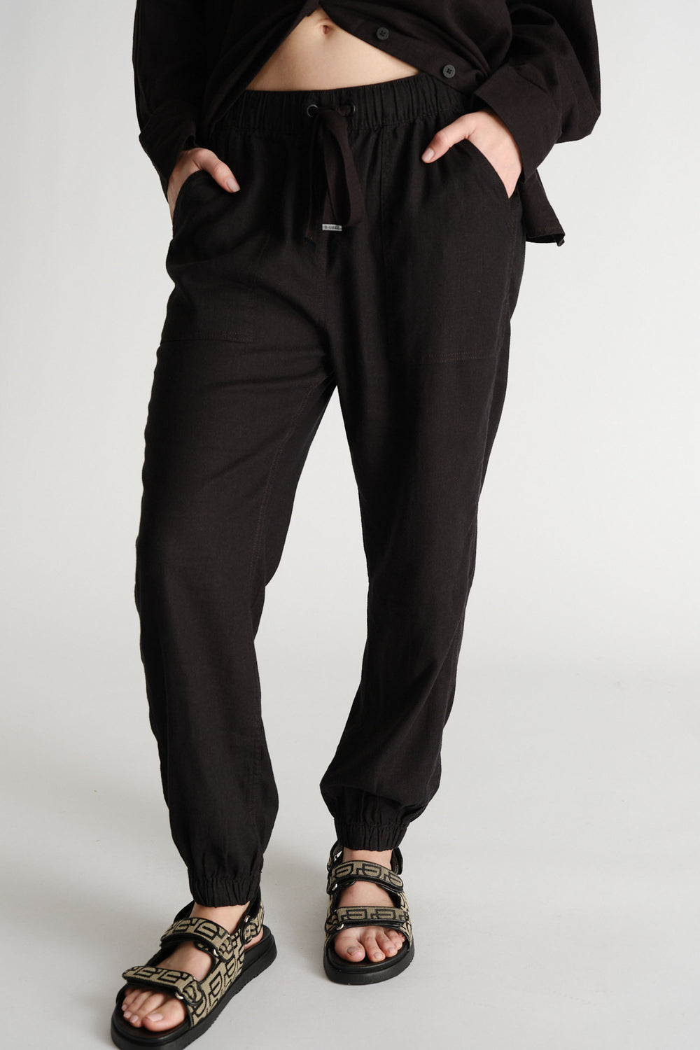 Woman wearing relaxed black linen-blend joggers with elastic cuffs and drawstring waist paired with patterned sandals