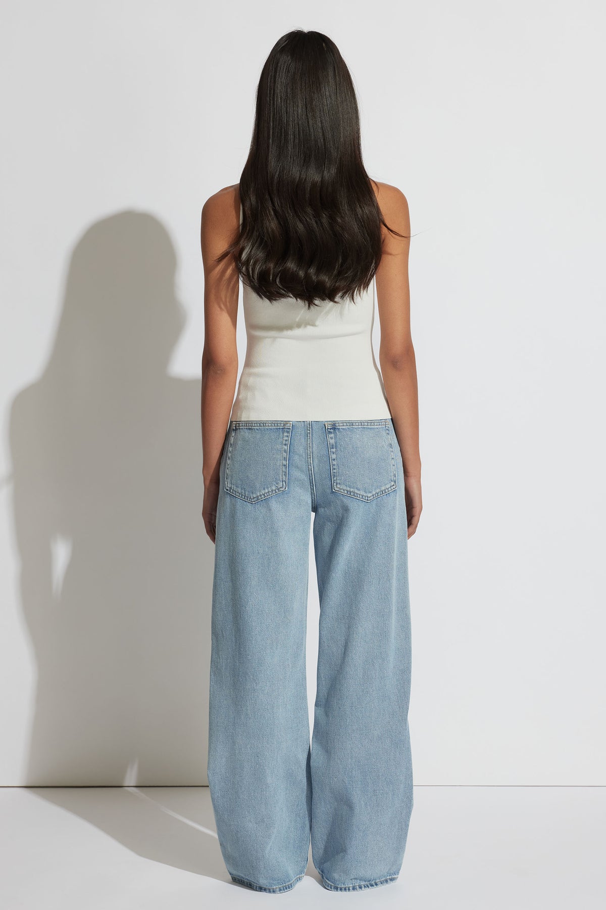 Woman seen from behind wearing an ivory square neck tank top paired with light blue wide-leg denim jeans