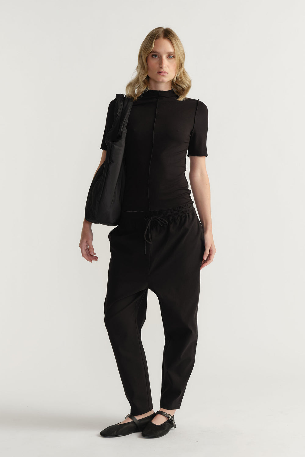 Woman wearing a fitted black short sleeve top with relaxed black pants and slip-on flats for a minimalist look