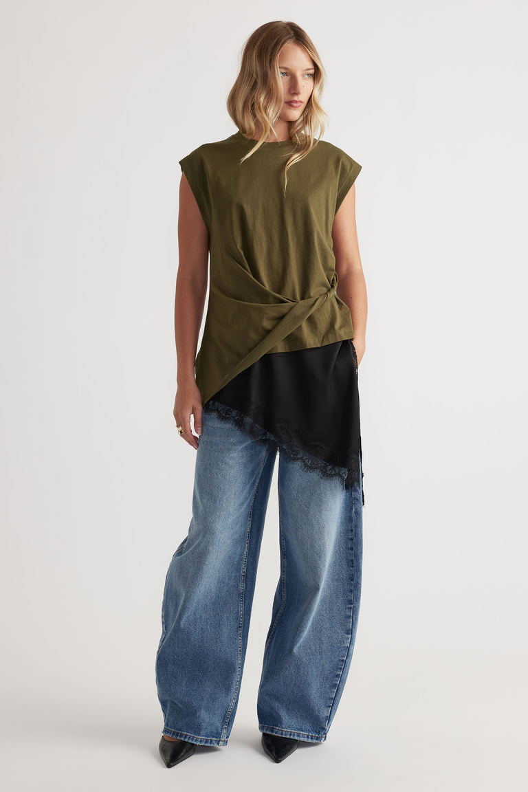 Woman wearing an olive twist-detail top paired with wide-leg blue jeans and black pointed shoes in a casual look