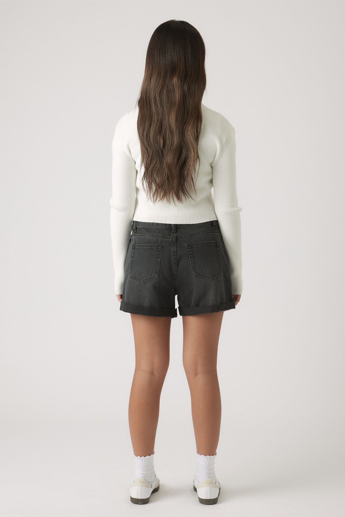 Girl wearing washed black cuffed denim shorts paired with a fitted long-sleeve white top for casual style.