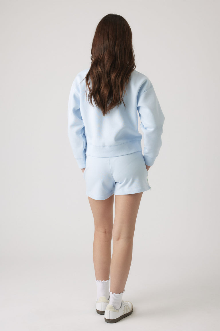 Teen girl in a pale blue sweat and matching shorts, paired with white ruffle socks and casual sneakers.