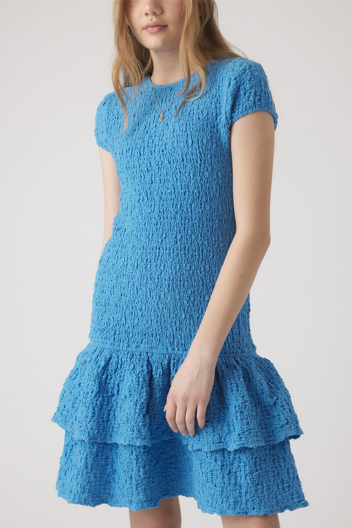 Girl wearing a textured bright blue short sleeve shirred dress with a tiered ruffle skirt detail