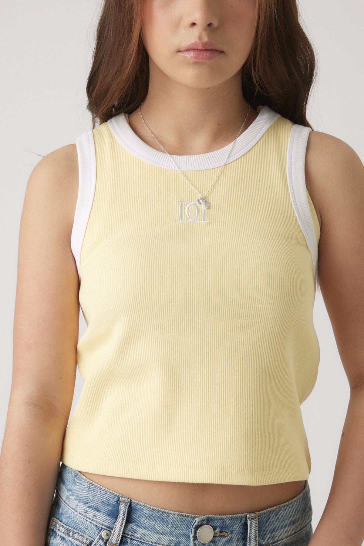 Close-up of girl wearing a pale yellow ribbed tank top with white trim, paired with light wash denim jeans.