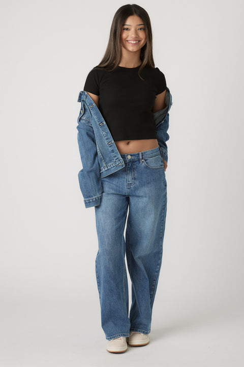 Teen girl wearing a black cropped tee and relaxed blue jeans, styled with a denim jacket casually draped off shoulders