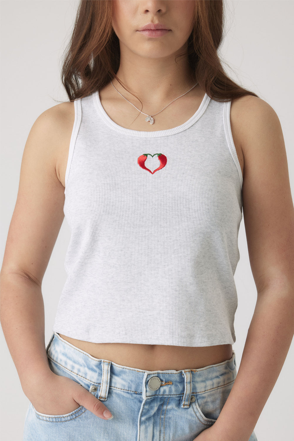 Girl wearing a white ribbed tank with a small embroidered red heart design, paired with light wash denim shorts.